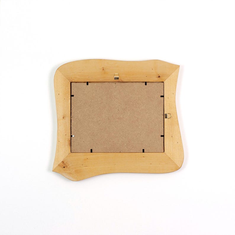 May include: A rectangular picture frame made of light-coloured natural wood with an irregular, wavy outer edge. The back of the frame features a brown fibreboard backing secured with small metal clips and two metal hanging hooks attached.