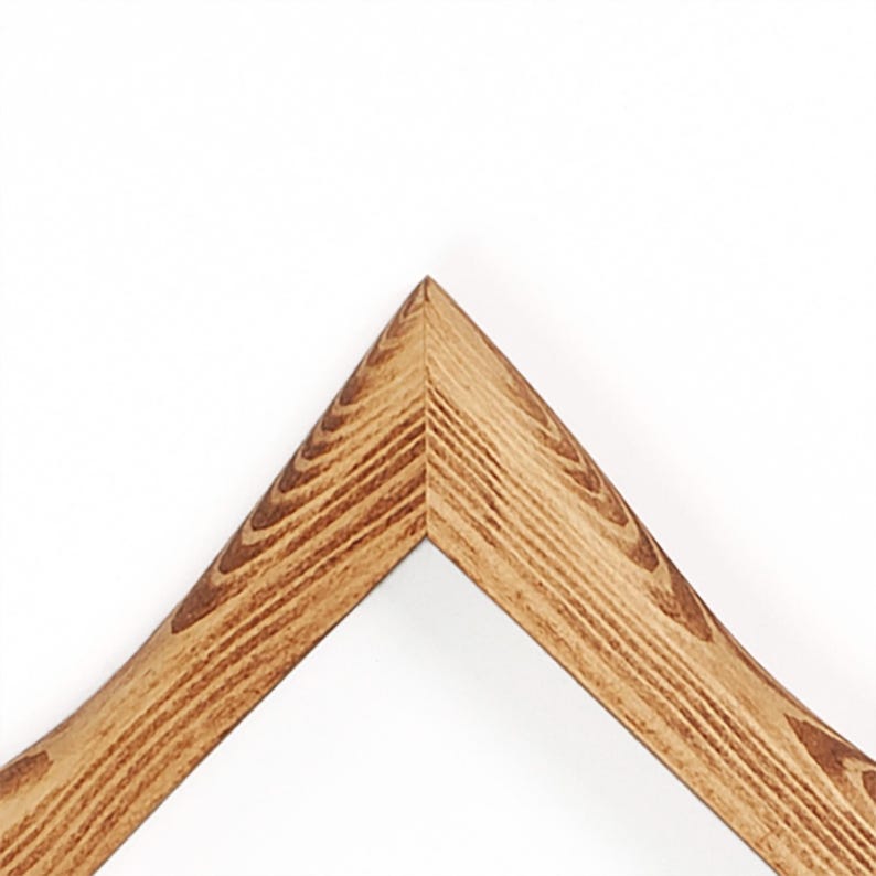 May include: A corner section of a wooden picture frame featuring a prominent natural wood grain pattern in shades of light and dark brown. The frame is joined at a sharp forty-five-degree angle, showcasing the texture and linear wood grain.