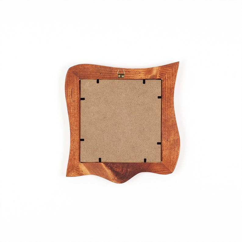 May include: A wooden picture frame with a distinctive, wavy edge design. The frame is a warm brown colour and has a square opening for a photo. Includes a metal hanger on the back for wall mounting.