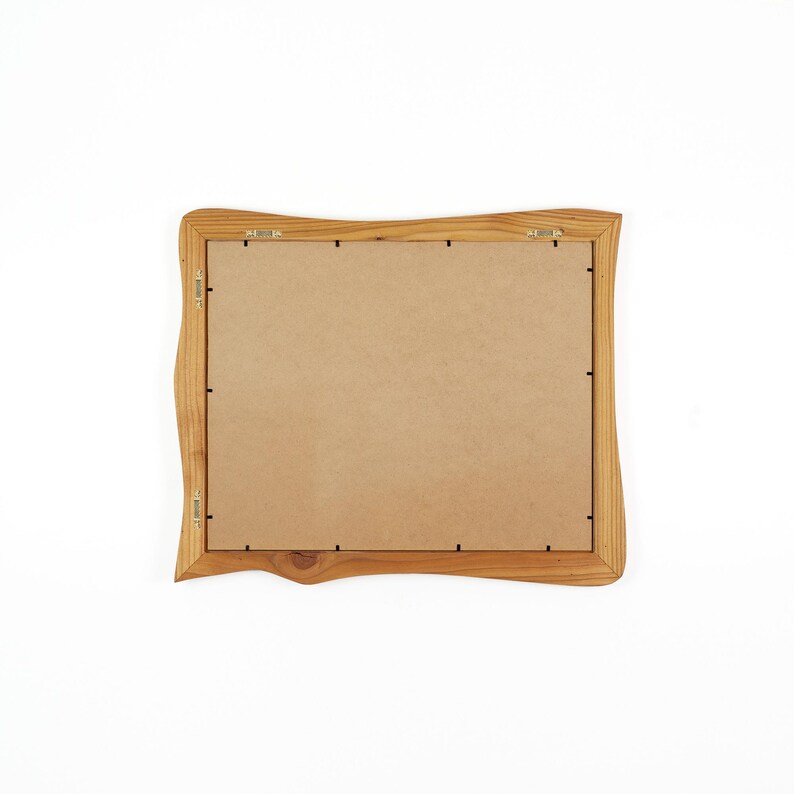 May include: A rectangular picture frame with a natural light brown wood finish and an irregular, wavy outer edge. The back of the frame features a flat, tan-colored backing board secured with metal clips and two metal hanging brackets attached.
