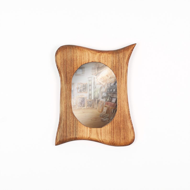 May include: A wooden picture frame with a distinctive, curved shape. The frame is crafted from light brown wood, showcasing the grain and a polished surface. An oval aperture displays a blurred image of an art gallery. The frame is a decorative item.