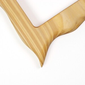 May include: Close-up of a wooden object with a curved, V-shaped design. The wood has a light brown color with visible grain patterns. The object's edges are smooth and rounded, with a pointed tip at the end of one arm.