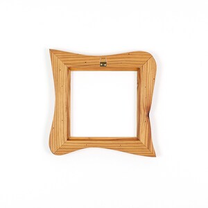 K&ouml;nnte beinhalten: Ein quadratischer Holzbilderrahmen mit einem einzigartigen, wellenf&ouml;rmigen Design. Der Rahmen besteht aus hellfarbenem Holz und hat einen Metallaufh&auml;nger auf der R&uuml;ckseite. Der Rahmen ist leer, mit einem wei&szlig;en Hintergrund, der durch die &Ouml;ffnung sichtbar ist.