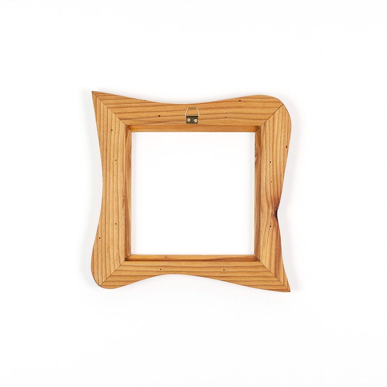K&ouml;nnte beinhalten: Ein quadratischer Holzbilderrahmen mit einem einzigartigen, wellenf&ouml;rmigen Design. Der Rahmen besteht aus hellfarbenem Holz und hat einen Metallaufh&auml;nger auf der R&uuml;ckseite. Der Rahmen ist leer, mit einem wei&szlig;en Hintergrund, der durch die &Ouml;ffnung sichtbar ist.