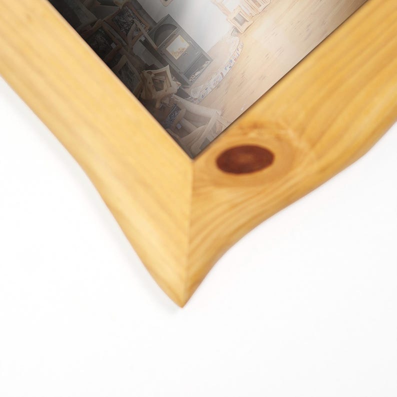 May include: A light-coloured wooden picture frame with a natural finish. The frame has a unique, curved design on the edges and a knot detail. The frame holds a picture with a blurred interior scene.