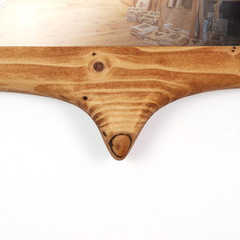 Pu&ograve; includere: Primo piano di una cornice in legno con finitura naturale venata. La cornice ha un design curvo unico con un dettaglio a nodo nella parte inferiore. La cornice &egrave; in legno marrone chiaro.