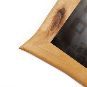 Peut inclure: Gros plan sur un cadre photo en bois avec une finition marron clair naturelle. Le cadre a un design incurv&eacute; unique avec un d&eacute;tail de n&oelig;ud. Le cadre est inclin&eacute;, mettant en valeur le coin et le verre.