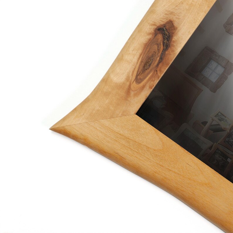 Peut inclure: Gros plan sur un cadre photo en bois avec une finition marron clair naturelle. Le cadre a un design incurv&eacute; unique avec un d&eacute;tail de n&oelig;ud. Le cadre est inclin&eacute;, mettant en valeur le coin et le verre.