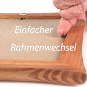 Peut inclure: Un cadre photo en bois avec le texte allemand "Einfacher Rahmenwechsel" en blanc. Le cadre est de couleur marron chaud et a un design simple et classique. Une main est montr&eacute;e en train d'ajuster le cadre.