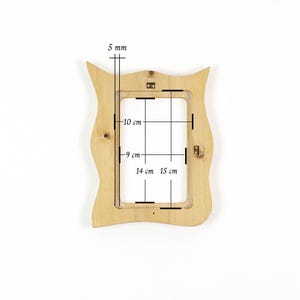 Pu&ograve; includere: Una cornice portafoto in legno chiaro con bordo esterno ondulato. La cornice presenta un'apertura rettangolare con dimensioni interne di 10 cm per 14 cm e dimensioni esterne di 15 cm per 9 cm, con uno spessore di 5 mm. Include ganci in metallo.
