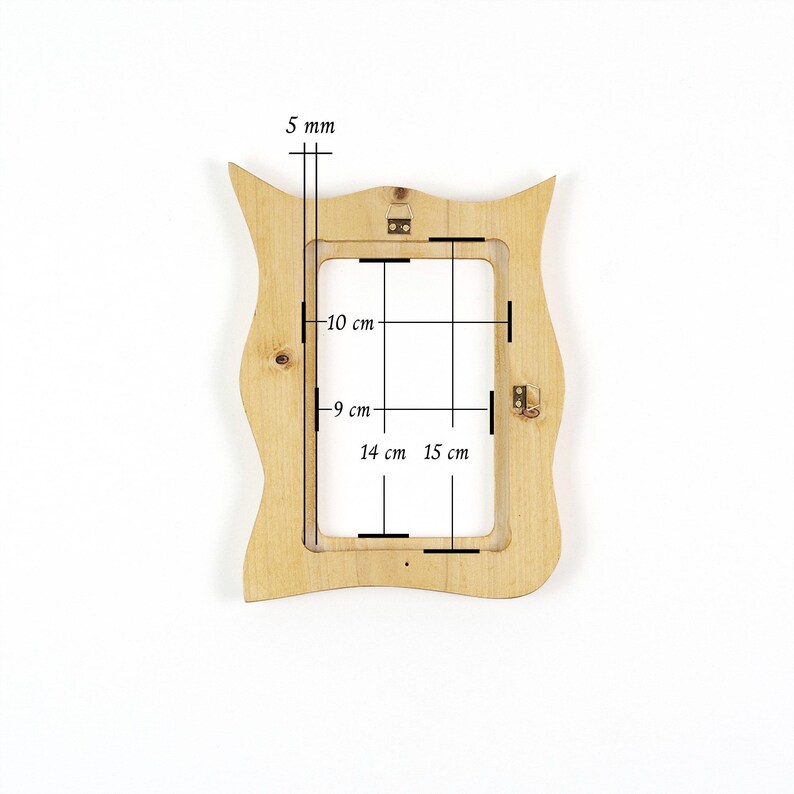 Pu&ograve; includere: Una cornice portafoto in legno chiaro con bordo esterno ondulato. La cornice presenta un'apertura rettangolare con dimensioni interne di 10 cm per 14 cm e dimensioni esterne di 15 cm per 9 cm, con uno spessore di 5 mm. Include ganci in metallo.