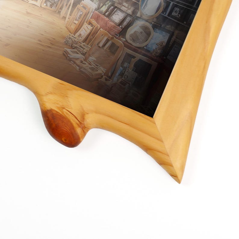 Peut inclure: Un cadre photo en bois clair avec un bord naturel brut pr&eacute;sentant un n&oelig;ud de bois fonc&eacute; pro&eacute;minent sur la traverse inf&eacute;rieure. Le cadre entoure une photographie repr&eacute;sentant un espace int&eacute;rieur avec divers cadres et objets en bois expos&eacute;s.