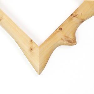 K&ouml;nnte beinhalten: Eine helle Holzrahmenecke mit einer V-f&ouml;rmigen Gehrungsverbindung. Das Holz weist eine nat&uuml;rliche Maserung mit sichtbaren &Auml;sten und eine glatte, polierte Oberfl&auml;che auf. Der Rahmen hat ein abgerundetes, ast&auml;hnliches Au&szlig;enprofil.