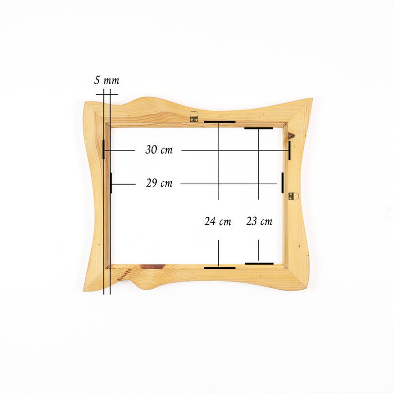 May include: A light-coloured wooden picture frame with an irregular, wavy outer edge. Technical lines and text indicate dimensions of 5 mm, 30 cm, 29 cm, 24 cm, and 23 cm. The frame features two small metal hanging brackets attached to the top and side.