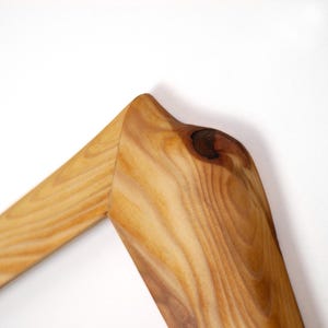 Puede incluir: Una secci&oacute;n de esquina de un marco de madera con un patr&oacute;n de veta de madera natural de color marr&oacute;n claro. La superficie muestra un detalle de nudo circular oscuro prominente cerca de la uni&oacute;n a inglete donde dos piezas de madera se unen.