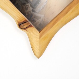 Peut inclure: Vue en coin d'un cadre photo en bois avec une finition naturelle. Le cadre a un design incurv&eacute; unique de couleur marron clair. Le cadre est vide, avec le reflet d'une pi&egrave;ce visible &agrave; l'int&eacute;rieur.