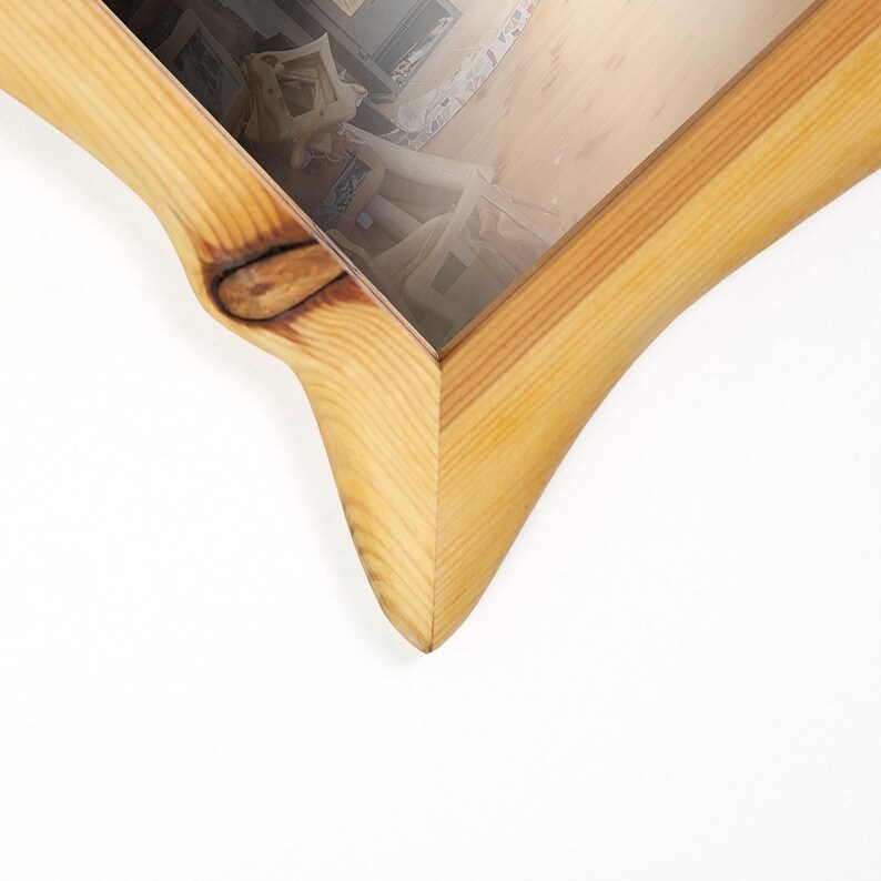 Peut inclure: Vue en coin d'un cadre photo en bois avec une finition naturelle. Le cadre a un design incurv&eacute; unique de couleur marron clair. Le cadre est vide, avec le reflet d'une pi&egrave;ce visible &agrave; l'int&eacute;rieur.