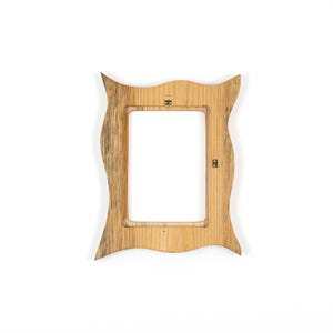 Pu&ograve; includere: Una cornice in legno dal design ondulato unico. La cornice &egrave; realizzata in legno chiaro con venature pi&ugrave; scure e presenta un'apertura rettangolare per una foto. Due ganci in metallo sono visibili sul retro.