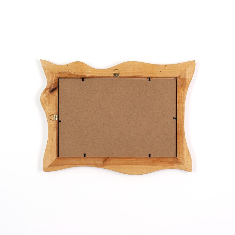 May include: A rectangular picture frame crafted from light-toned natural wood with an irregular, wavy outer edge. The back of the frame features a flat brown backing board secured with metal clips and includes two metal hanging hooks attached.