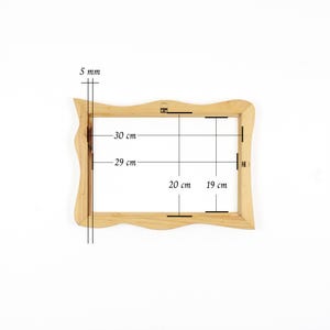 May include: A light-coloured wooden picture frame with wavy outer edges. The frame features technical markings indicating dimensions of 30 cm by 20 cm, an inner opening of 29 cm by 19 cm, and a frame thickness of 5 mm, with metal hanging hardware.