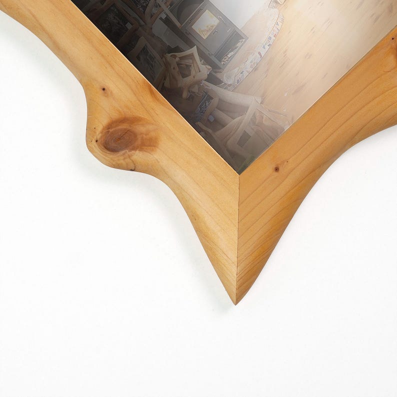 May include: A wooden picture frame with a unique, organic shape. The frame is made of light-colored wood, featuring a natural grain and a knot detail. The frame's design includes curved edges and a pointed corner, creating a distinctive look.