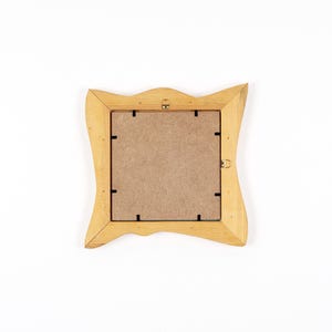Peut inclure: Dos d'un cadre photo en bois brun clair avec un design ondul&eacute; unique. Le cadre a une ouverture carr&eacute;e et un dos en carton. Le cadre est pos&eacute; sur un fond blanc.