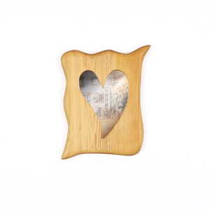 May include: A wooden picture frame with a heart-shaped cutout. The frame has a natural wood grain finish and a unique, wavy edge design. The heart-shaped opening reveals a glimpse of the image within.