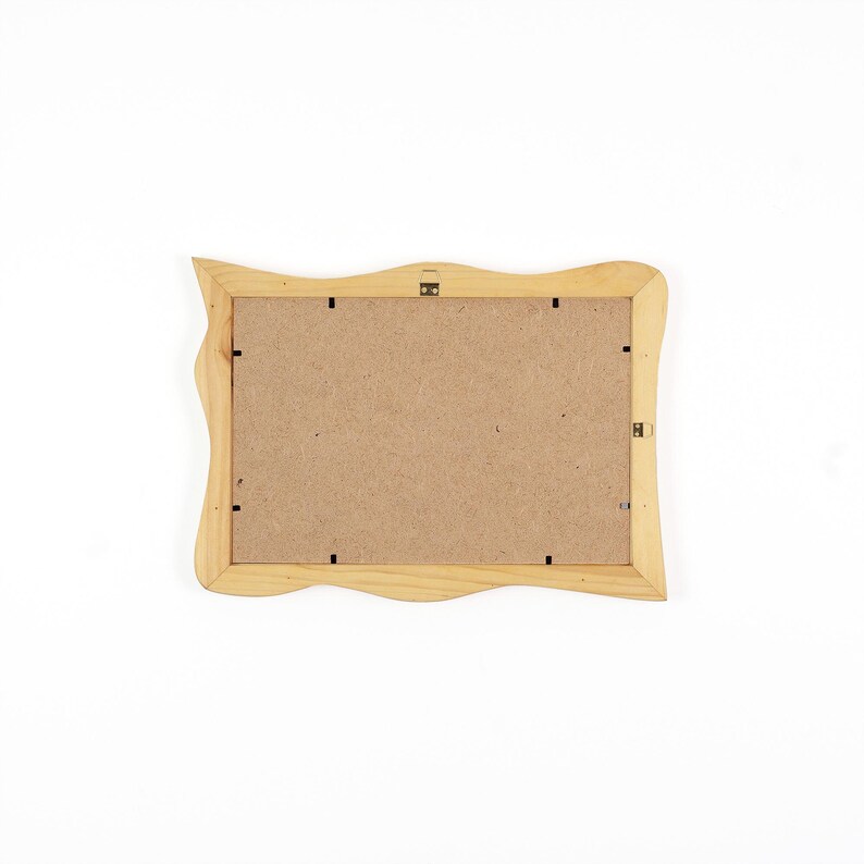 May include: A rectangular wooden picture frame shown from the back, featuring a light natural wood finish with wavy, organic edges. The centre is filled with a flat, brown fibreboard backing secured by small metal clips and a metal hanging bracket.