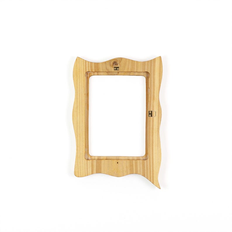 May include: A light-colored wooden picture frame with a wavy, irregular border. The frame has a rectangular opening and hardware for hanging. The wood grain is visible, and the frame is set against a white background.