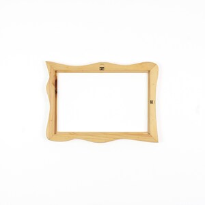 May include: A rectangular wooden picture frame with a natural light brown finish and wavy, organic edges. The frame features two small metal hanging brackets attached to the inner wooden border, allowing for horizontal or vertical wall mounting.