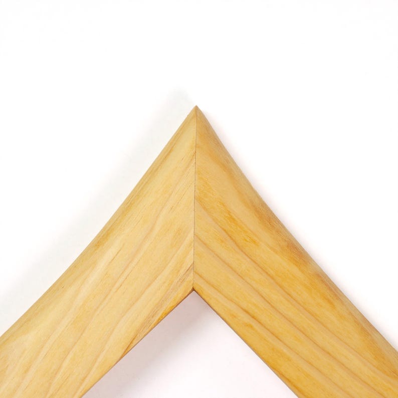 Puede incluir: Una secci&oacute;n de esquina de un marco de fotos de madera de color claro con una uni&oacute;n a inglete. La madera muestra un patr&oacute;n de veta natural con vetas de color marr&oacute;n claro visibles y una superficie lisa e inclinada que se une en una punta.