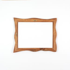May include: A wooden picture frame with a natural, wavy edge. The frame is a warm brown color and has a rectangular opening. Small metal hangers are attached to the back for hanging. The frame is designed to hold a photograph or artwork.