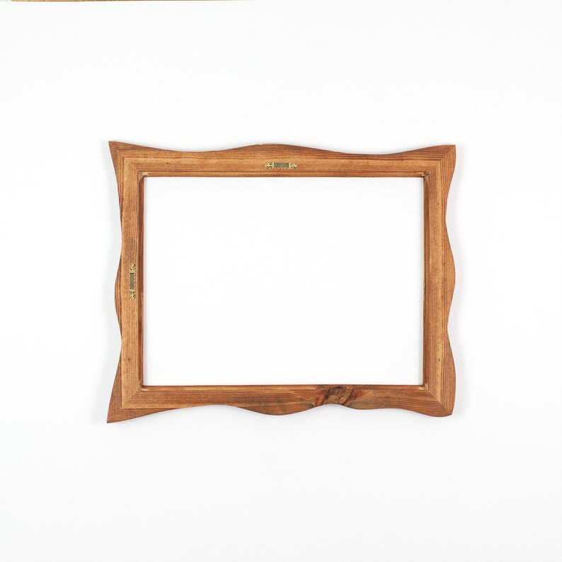 May include: A wooden picture frame with a natural, wavy edge. The frame is a warm brown color and has a rectangular opening. Small metal hangers are attached to the back for hanging. The frame is designed to hold a photograph or artwork.
