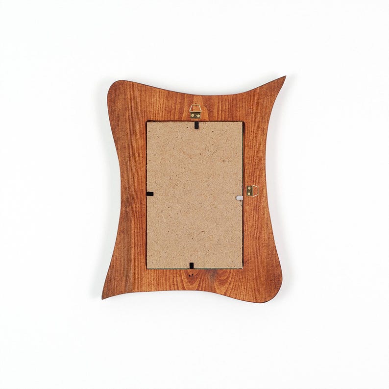 May include: Rear view of a wooden picture frame with a distinctive, undulating shape. The frame is a warm brown hue, featuring a rectangular aperture for a photograph. The back has a cardboard backing and metal hanging hardware.