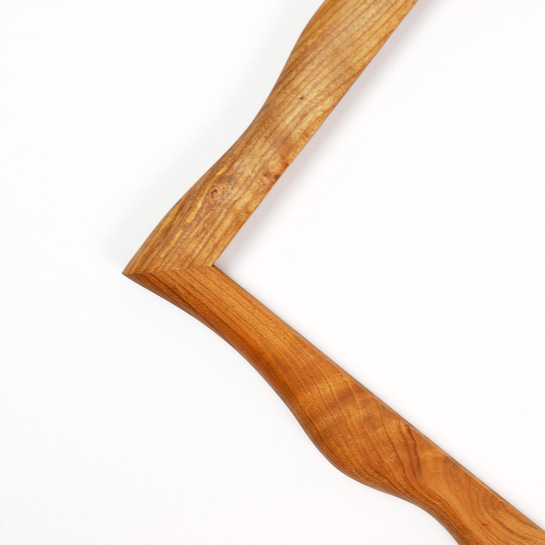 Pu&ograve; includere: Vista parziale di una cornice in legno, che mostra la sua venatura naturale e le tonalit&agrave; calde. La cornice ha un design curvo unico, con un angolo visibile. Il legno &egrave; marrone chiaro, con motivi di venatura visibili.
