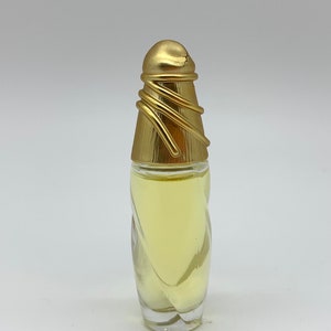 Puede incluir: Una botella de perfume de vidrio transparente con una tapa dorada y un diseño retorcido. La botella está llena de un líquido amarillo claro.