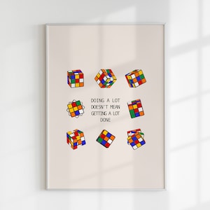 May include: A motivational poster with a beige background featuring a quote about productivity. The quote reads "Doing a lot doesn't mean getting a lot done." The quote is surrounded by colourful Rubik's cubes in various positions.