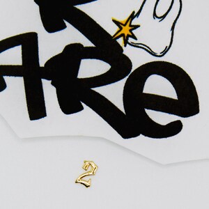 May include: Gold-colored number two charm with a gothic font style. The charm is on a white background.