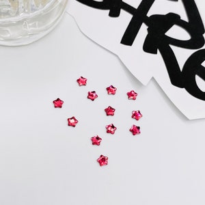 May include: A scattering of small, pink, star-shaped rhinestones on a white surface.