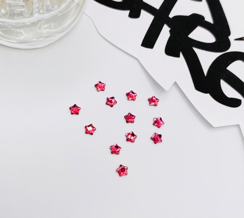 May include: A scattering of small, pink, star-shaped rhinestones on a white surface.