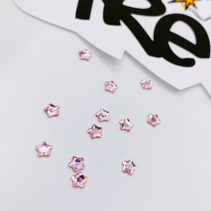 May include: A scattering of pink star-shaped rhinestones on a white surface.