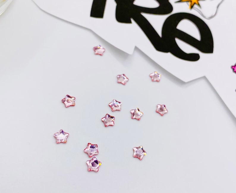 May include: A scattering of pink star-shaped rhinestones on a white surface.