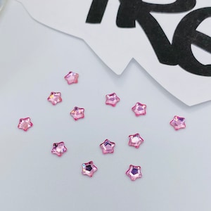 May include: A scattering of pink star-shaped rhinestones on a white surface.