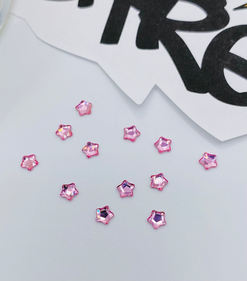 May include: A scattering of pink star-shaped rhinestones on a white surface.