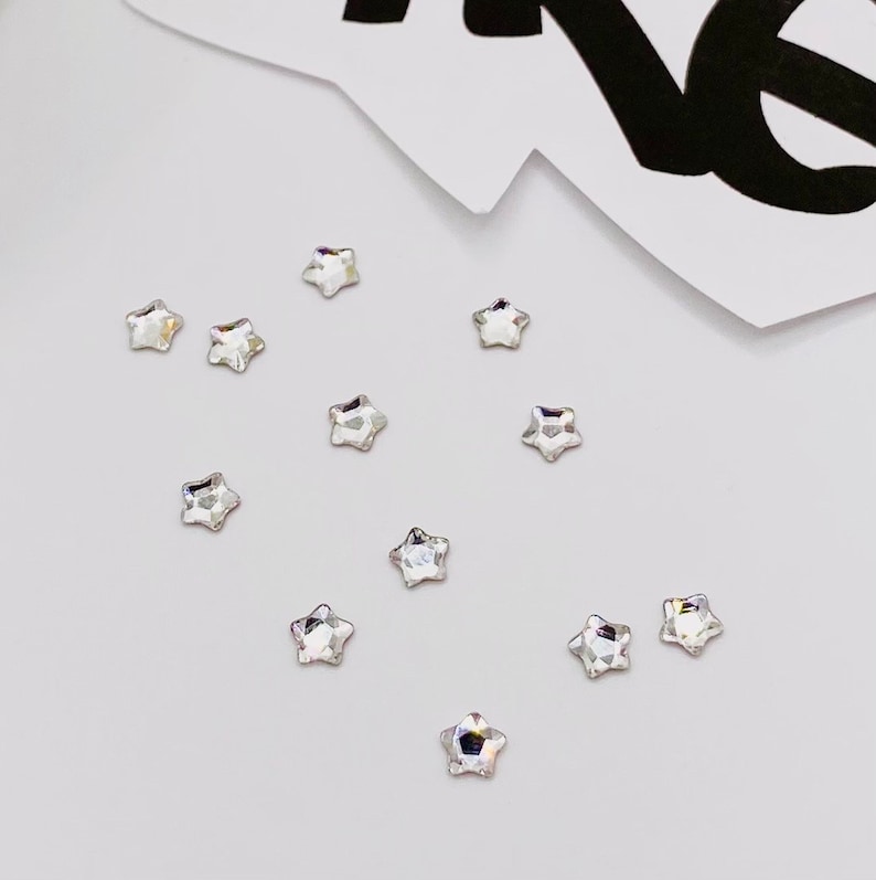 May include: A collection of small, clear star-shaped rhinestones scattered on a white surface.