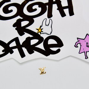 May include: A gold-colored letter Y charm with a white background. The background has a black and white illustration of a tooth with a star and the words "goth r care".