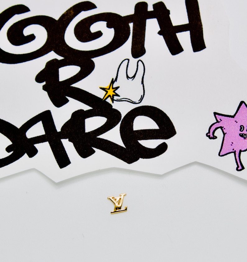 May include: A gold-colored letter Y charm with a white background. The background has a black and white illustration of a tooth with a star and the words "goth r care".