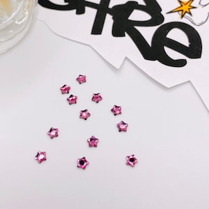 May include: A scattering of pink star-shaped rhinestones on a white surface.