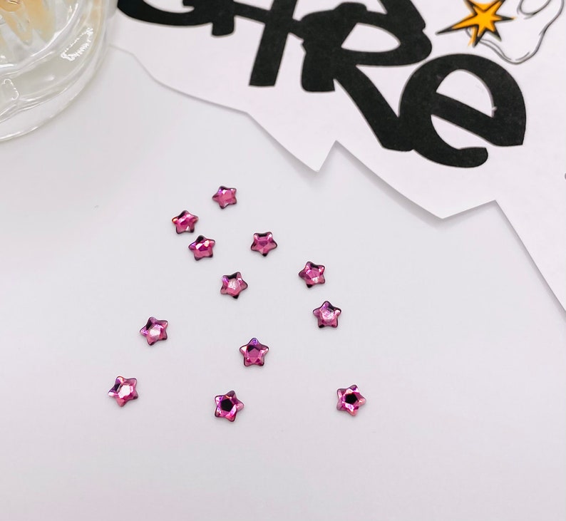 May include: A scattering of pink star-shaped rhinestones on a white surface.