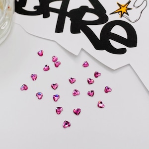 May include: A scattering of pink heart-shaped rhinestones on a white surface.